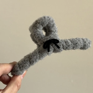 Pince à cheveux en peluche grise avec nœud en velours noir tenue sur fond beige doux