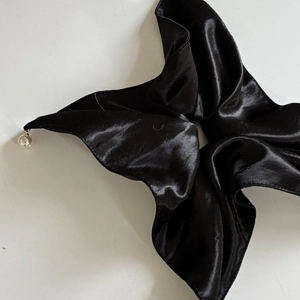 Detail view of smooth black satin scrunchie with elegant hanging white pearl accents