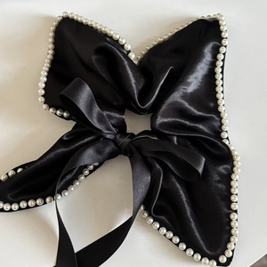 Detail of a black satin bow hair tie featuring a hand-stitched faux pearl border trim