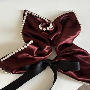 Detail of red satin bow hair accessory with white pearl trim and black ribbon tail