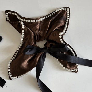 Close-up of brown satin hair scrunchie with faux pearl edges and a black bow accent