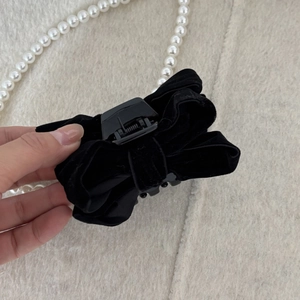 Detailed view of the soft black velvet bow hair claw clip held by hand over felt fabric