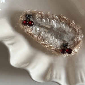 Detail of crochet hair clip with red cherry beads on a decorative shell plate