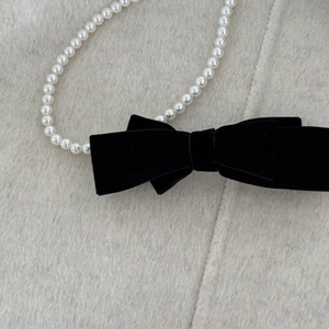 Detailed macro of black velvet bow hair clip with elegant white pearl chain accents