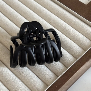 Detailed close-up of matte black hair claw clip with strong metal spring on beige tray