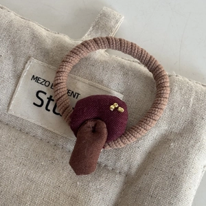 Detail eines handgemachten Haargummis mit braunem Stoffpilz und Goldperlen auf Leinwand