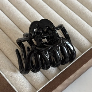 Close-up of glossy black hair claw clip with double C design on beige velvet stand