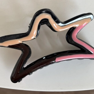 Detail of star-shaped hair claw clip with black finish and pink wave enamel accents