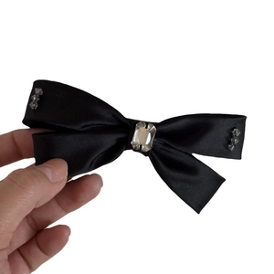 Barrette à nœud en satin noir élégante avec strass en cristal tenue à la main sur blanc