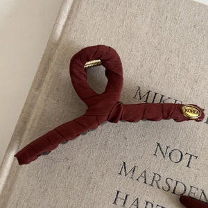 Detail of burgundy twill fabric wrapped hair claw clip with golden Korea logo plate