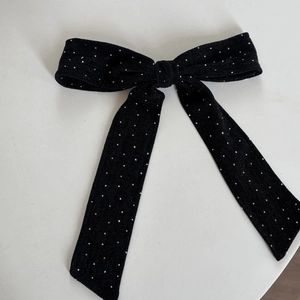 Detail of black bow hairclip with shimmering fabric and silver rhinestones on white background