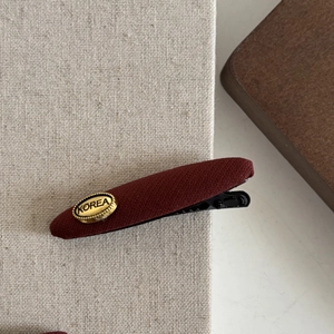 French style wine red twill hair clip with gold Korea emblem on beige linen background