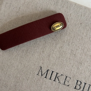 Detailed macro of burgundy twill fabric hair clip with a vintage gold brand tag