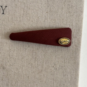 Detail of burgundy twill hair clip with golden metal KOREA tag on beige background