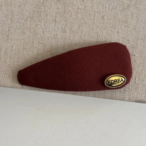 Macro detail of wine red twill fabric hair clip with a gold oval Korea metal logo