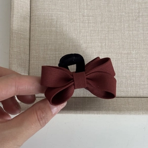 Macro detail of wine red ribbed fabric bow hair clip featuring an elegant golden label
