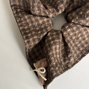 Macro shot of dark brown checkered scrunchie with seersucker texture and a mini plush bear