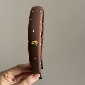 Detailed view of handmade vintage polka dot headband with golden metal brand logo