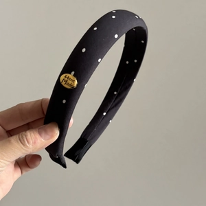 Detailed view of polka dot headband with golden 'Hand Made' plate and ribbon wrap edges