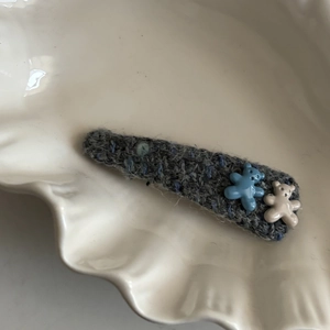 Cute knitted hair clip with blue and beige resin bears on white ceramic tray