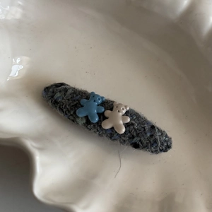 Detailed view of handmade knitted hair clip with cute bear charms on white ceramic plate