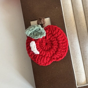 Handmade crochet red apple hair clip with green leaves on natural textured background