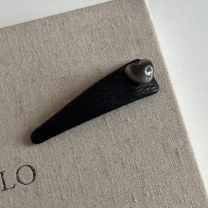 Minimalist black faux leather hair clip with shiny heart shaped embellishment on beige base