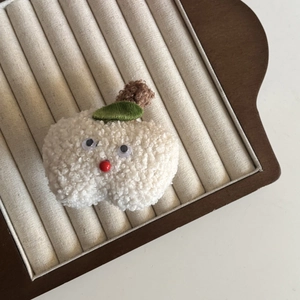 Handmade white sherpa apple hair accessory with cute cartoon face on a jewelry tray