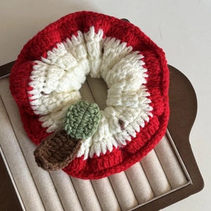 Detail of handmade crochet red apple hair scrunchie with intricate knit texture and leaf