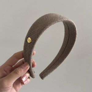 Detail of coffee brown herringbone fabric headband with round gold engraved metal plate
