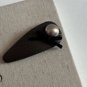 Detailed close-up of brown leather drop hair clip with black bow and grey pearl accent