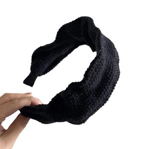Thick black knitted headband for women, stylish winter accessory held on white background