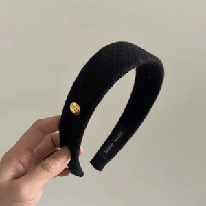 Detailed close-up of thick black tweed headband featuring a gold believe engraving metal plate