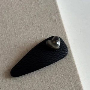 Close-up of black faux leather triangular hair clip with grey resin heart detail