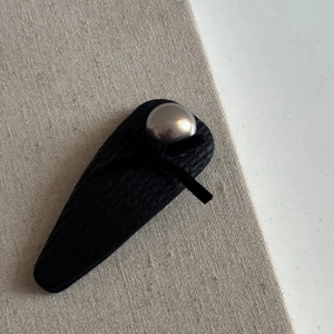 Macro shot of black textured BB hair clip with grey pearl accent on a linen background