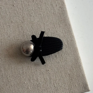 Close-up of elegant black velvet bow hair clip with chic cat-eye pearl on beige texture