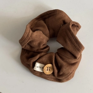 Detailed view of a soft brown pleated scrunchie featuring a wooden button and textile label