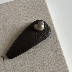 Macro detail of a coffee brown leather teardrop hair clip with a heart shaped pearl accent