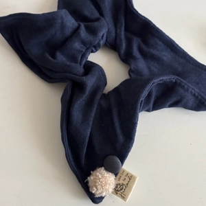 Close-up of handmade blue knit hair accessory with button detail and beige pom-pom
