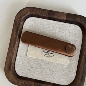 Macro detail of a dark brown satin hair clip featuring a velvet heart on a wooden tray