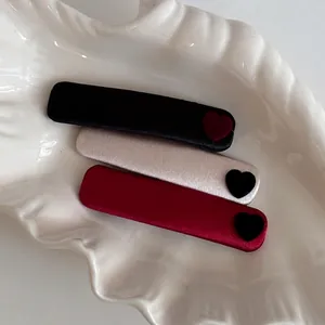 Three velvet heart hair clips in black, beige, and red colors on a white shell tray