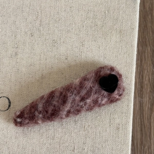 Detailed close-up of a dusty pink faux fur heart hair clip on a beige fabric background