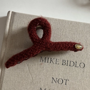 Detailed close-up of a burgundy wool hair clip with a vintage golden KOREA logo tag