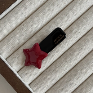 Detailed macro of red star hair clip with gold France Handmade logo on ivory texture