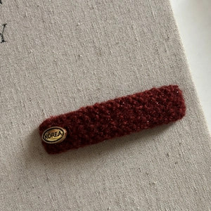 Close-up of a wine red tweed hair clip featuring a golden oval metal tag with Korea engraving