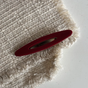 French style hollow oval hair clip in matte deep red resin on a woven background
