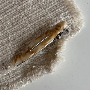 Detail view of oval acetate hair clip featuring a marble texture and silver metal base