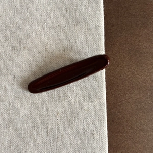 Vue détaillée d'une pince à cheveux ovale marron foncé poli sur un fond en toile épuré