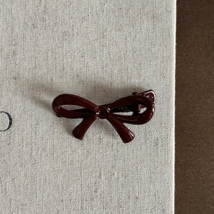 Détail macro d'une pince à cheveux nœud rouge bordeaux brillant sur fond de toile épuré