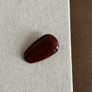 Détail de la barrette goutte rouge bordeaux avec fini brillant sur un fond en tissu texturé